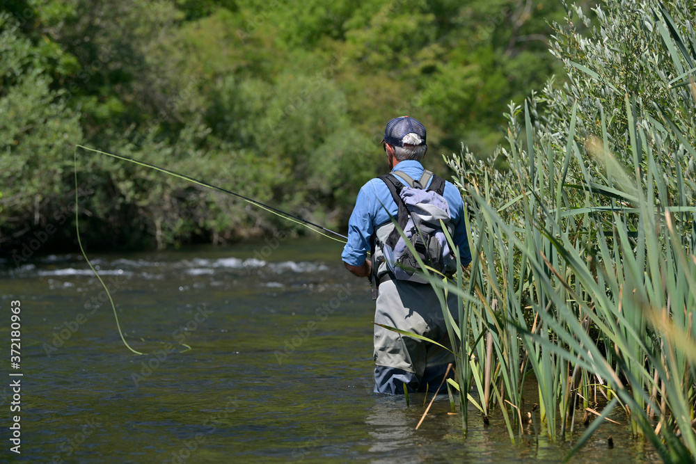 fly fisherman in summer fishing in a mountain river with waders and a cap fly fisherman in summer fishing in a mountain river with waders and a cap