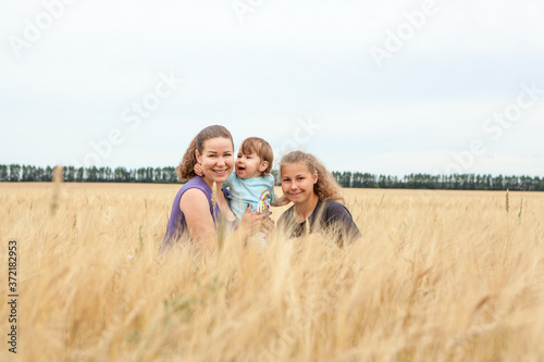 Caucasian single mother with her teenage girl and toddler child sitting in yellow wheat stems, smiling and looking at camera