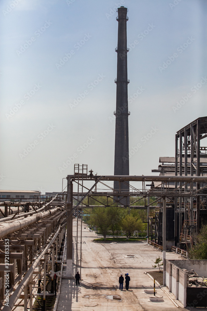 Plant chimney (smoking stack) and the pipelines of chemical factory on the grey sky. Phosphoric fertilizers plant.