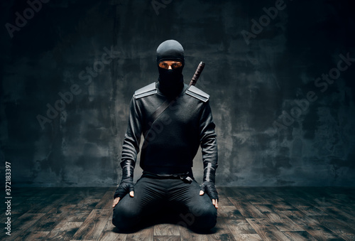 Vászonkép Ninja kneeling posing with a sword over black background