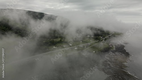 Looking through Gloomy Fog Over the Quaint Green Coastal Chic-Chocs Village, Drone Orbit with Tilt Down photo