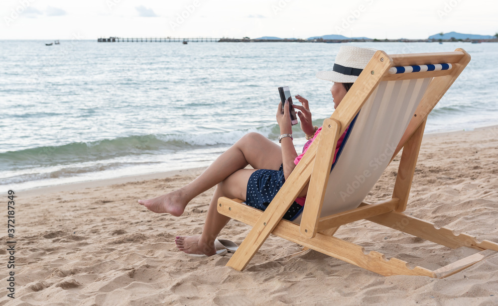Obraz premium Young woman using a mobile phone on the beach chair on vacation.