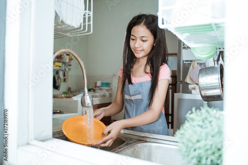 Obraz na plátně Portrait of asian teen girl doing household chores washing dishes in kitchen sin