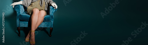 cropped view of fashionable pregnant woman sitting with crossed legs in velour armchair on dark blue, panoramic shot