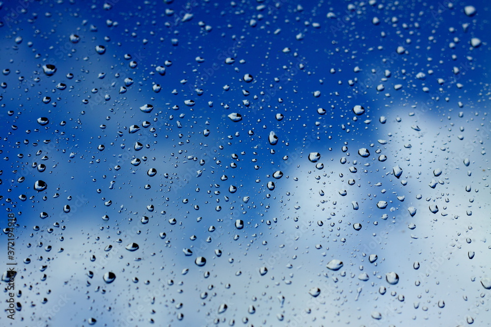 Water drops after rain on the glass. Blue sky and white clouds through the glass. Wallpaper, texture and postcard.