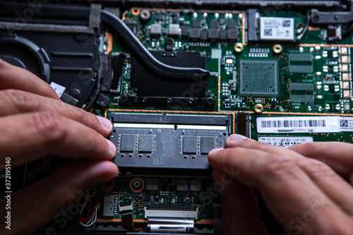 Close-up on the RAM memory that the hands of the service technician insert into the slot on the laptop computer.