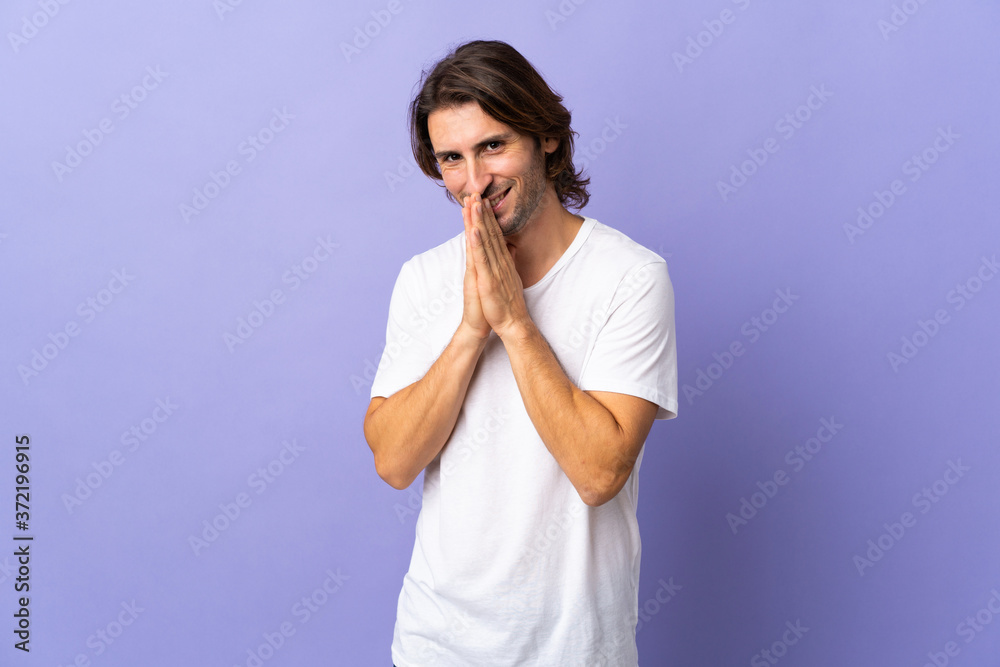 Young handsome man isolated on purple background keeps palm together. Person asks for something Young handsome man isolated on purple background keeps palm together. Person asks for something