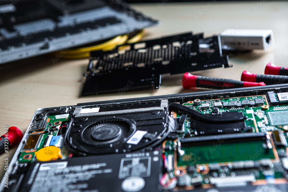 Disassembled laptop on the desktop. There are tools and various spare parts around it. Disassembled laptop on the desktop. There are tools and various spare parts around it.