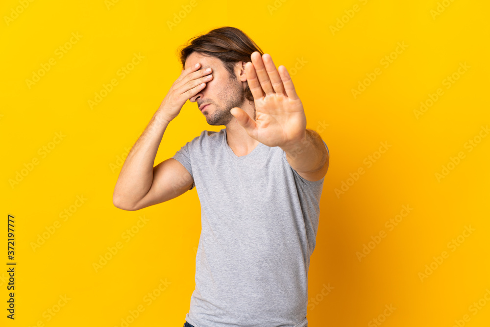 Young handsome man isolated on yellow background making stop gesture and covering face Young handsome man isolated on yellow background making stop gesture and covering face