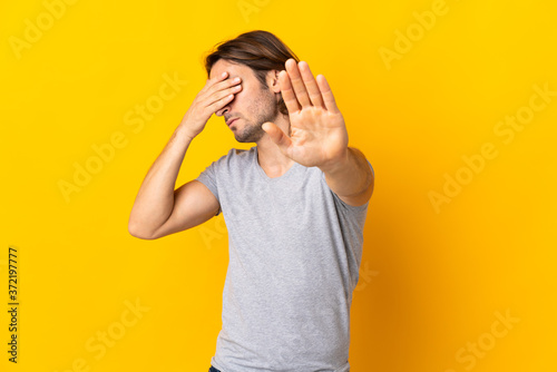 Young handsome man isolated on yellow background making stop gesture and covering face
