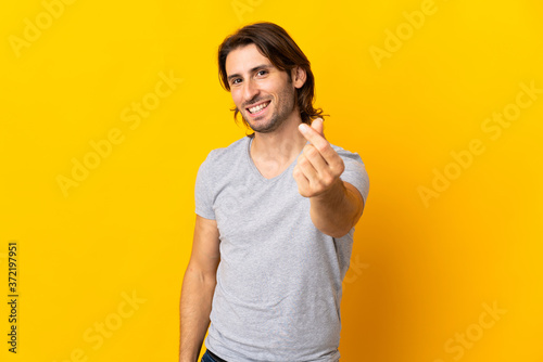 Young handsome man isolated on yellow background making money gesture © luismolinero