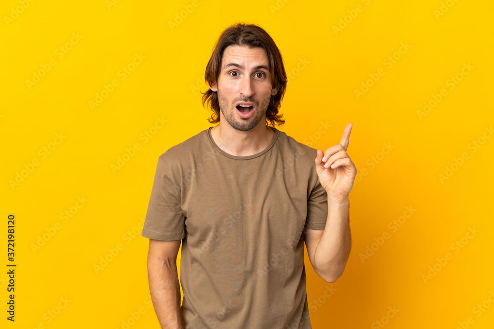 Young handsome man isolated on yellow background intending to realizes the solution while lifting a finger up Young handsome man isolated on yellow background intending to realizes the solution while lifting a finger up