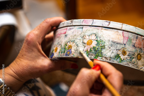 The hand of a woman who makes a decoupage with a brush on a round jewelry box. photo
