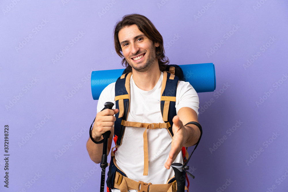 Young mountaineer man with a big backpack over isolated background shaking hands for closing a good deal Young mountaineer man with a big backpack over isolated background shaking hands for closing a good deal