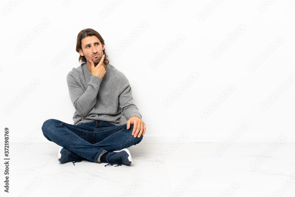 Young handsome man sitting on the floor over isolated background having doubts