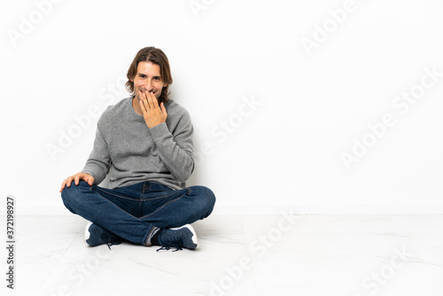 Young handsome man sitting on the floor over isolated background happy and smiling covering mouth with hand © luismolinero