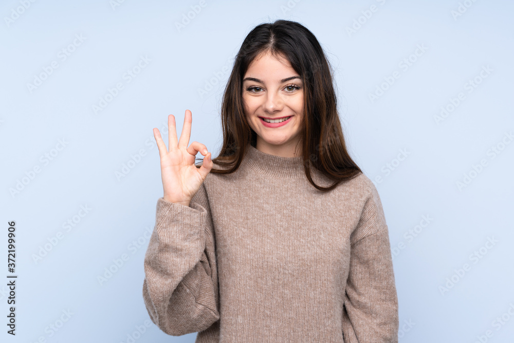 Young brunette woman wearing a sweater over isolated blue background showing ok sign with fingers Young brunette woman wearing a sweater over isolated blue background showing ok sign with fingers