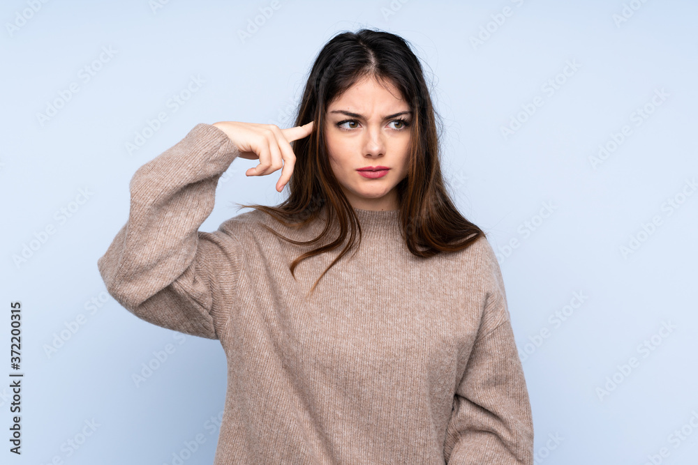 Young brunette woman wearing a sweater over isolated blue background making the gesture of madness putting finger on the head