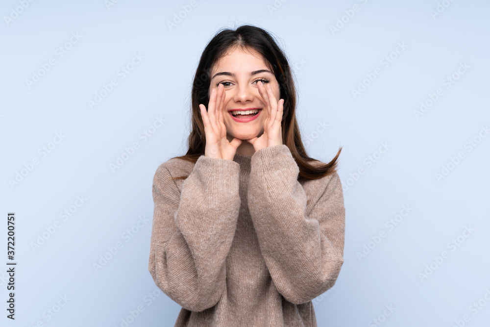 Young brunette woman wearing a sweater over isolated blue background shouting and announcing something Young brunette woman wearing a sweater over isolated blue background shouting and announcing something