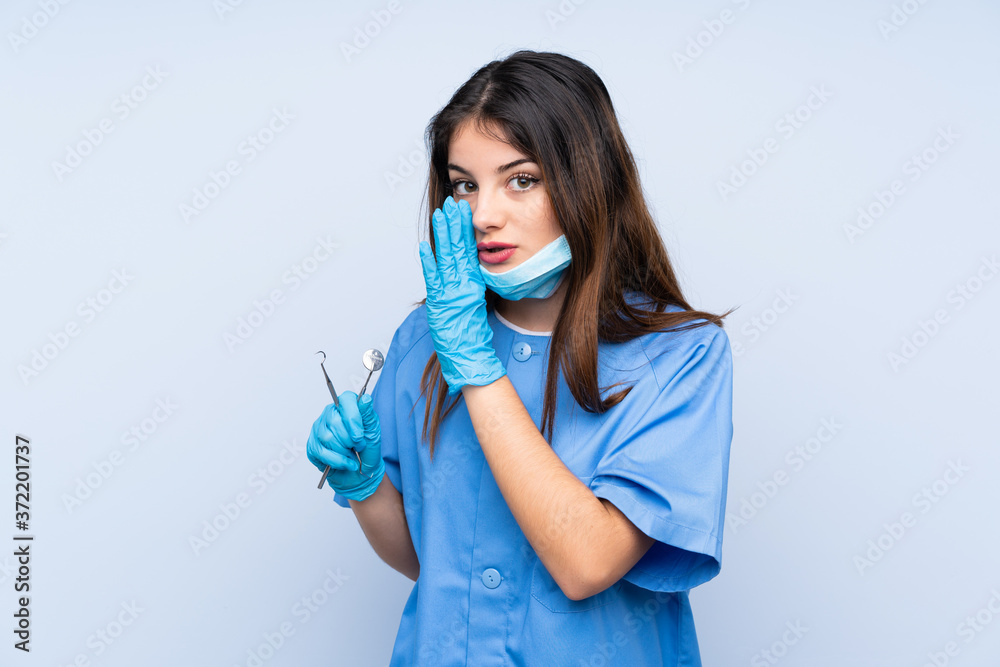 Woman dentist holding tools over isolated blue background whispering something Woman dentist holding tools over isolated blue background whispering something