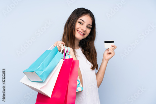 Young brunette woman over isolated blue background holding shopping bags and a credit card