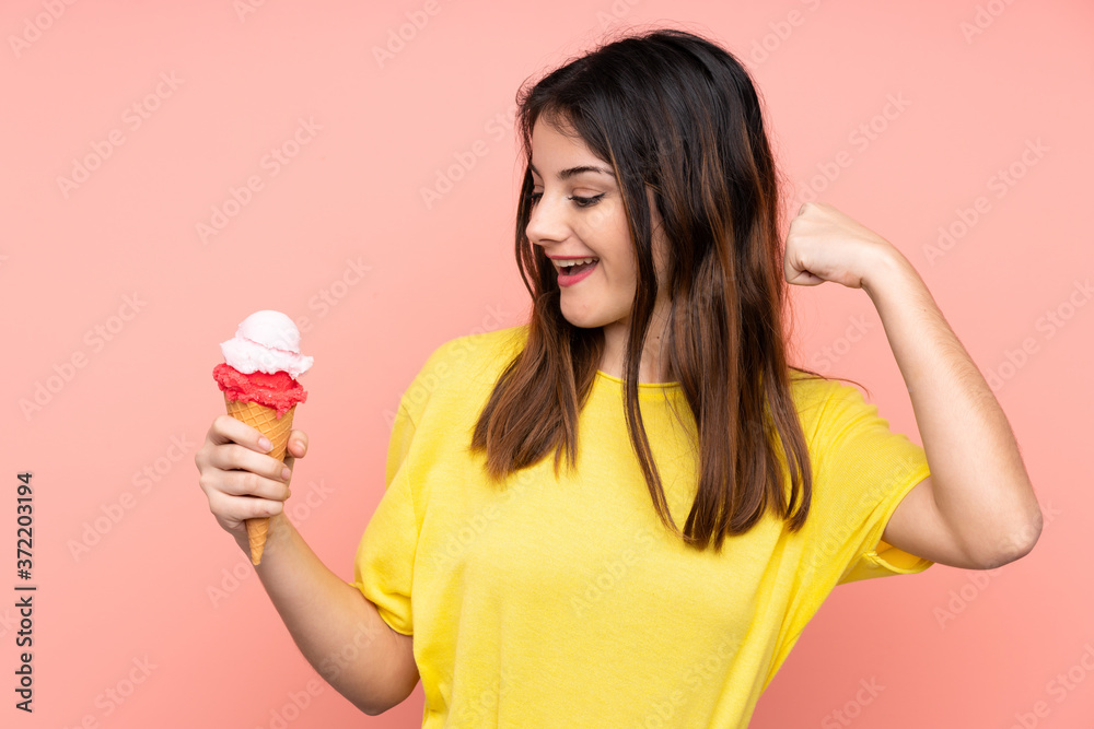 Young brunette woman holding a cornet ice cream over isolated pink background celebrating a victory Young brunette woman holding a cornet ice cream over isolated pink background celebrating a victory