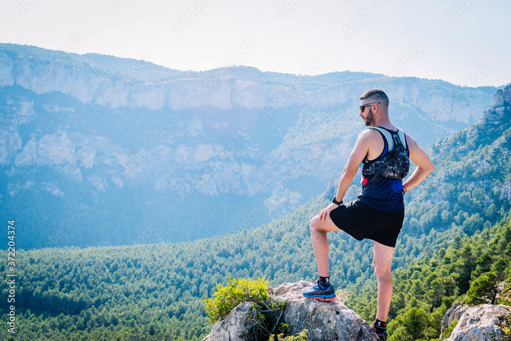 Naklejka premium Runner man up on a mound of rocks looking at the mountains.