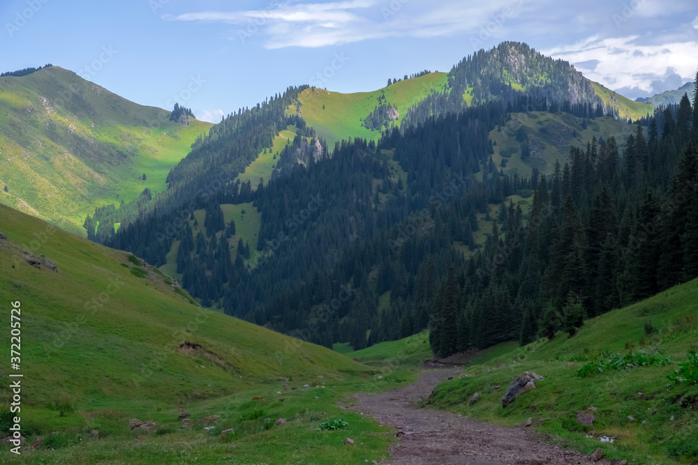 Beautiful view of green mountains with dangerous gravel road. Ketmen or Ketpen mountains gorge and mountain pass. Tourism in Kazakhstan.