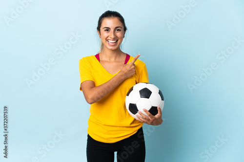 Young hispanic football player woman over isolated on blue background pointing to the side to present a product © luismolinero