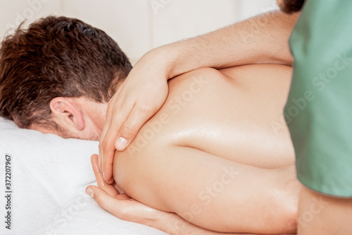 Close-up of massage therapist hands doing wellness massage on man shoulder in spa.