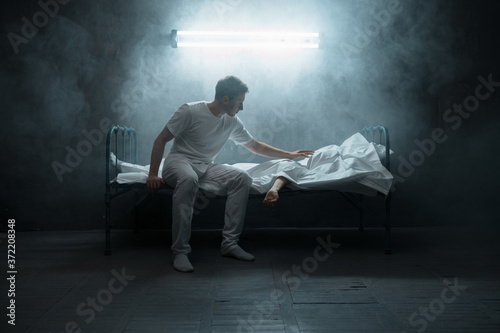 Sad psycho man looking on dead woman in bed