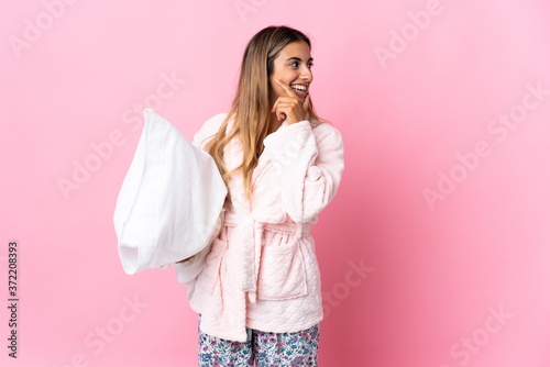 Young hispanic woman over isolated pink background in pajamas and thinking an idea while looking side
