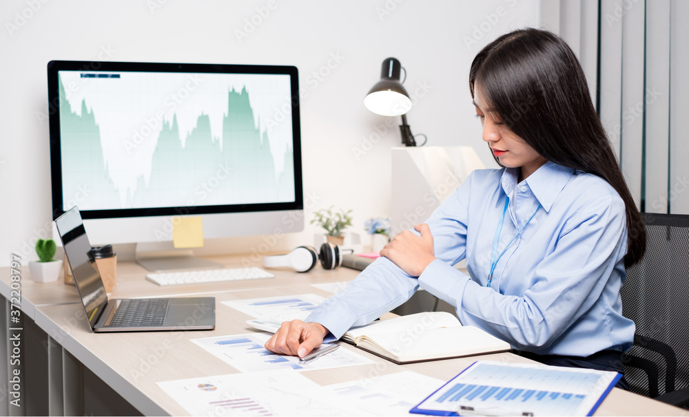 Asian female accountant is tired from of working in a chair, stretching, and massaging her arms for relaxation while working hard at the office Asian female accountant is tired from of working in a chair, stretching, and massaging her arms for relaxation while working hard at the office
