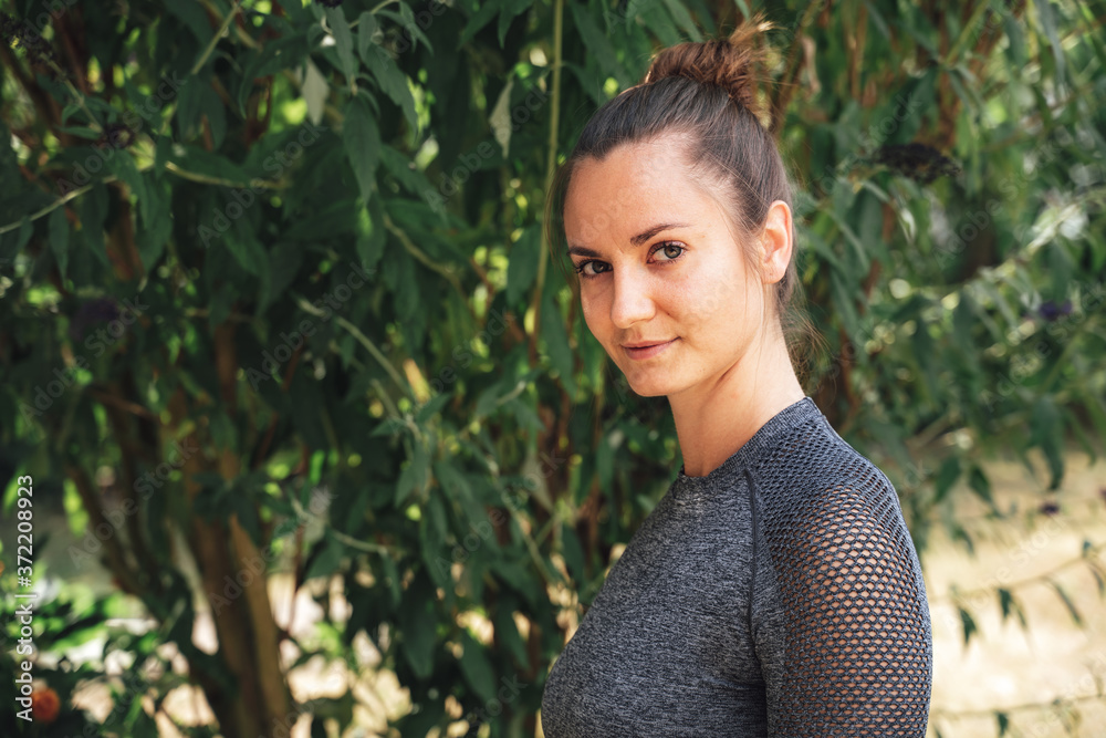 Close up portrait of confident young woman in sports clothing against plants in park