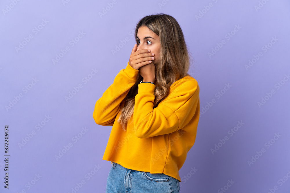 Young hispanic woman over isolated purple background covering mouth and looking to the side Young hispanic woman over isolated purple background covering mouth and looking to the side