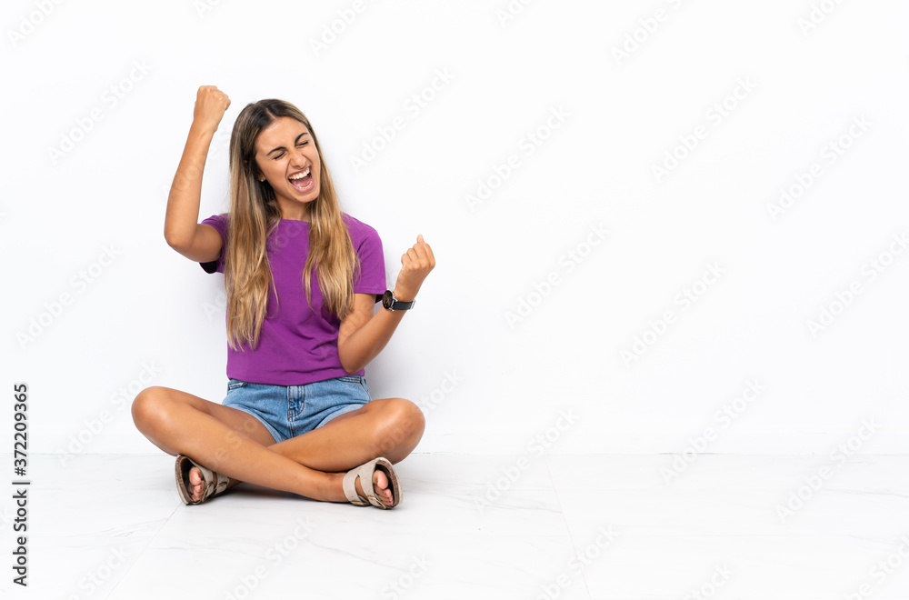 Young hispanic woman sitting on the floor celebrating a victory Young hispanic woman sitting on the floor celebrating a victory