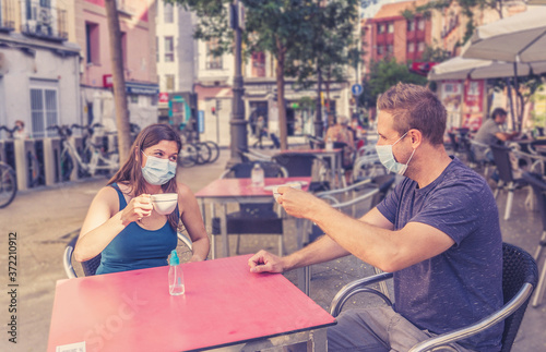 Couple sitting in a coffee bar with surgical masks in the New Normal after coronavirus pandemic