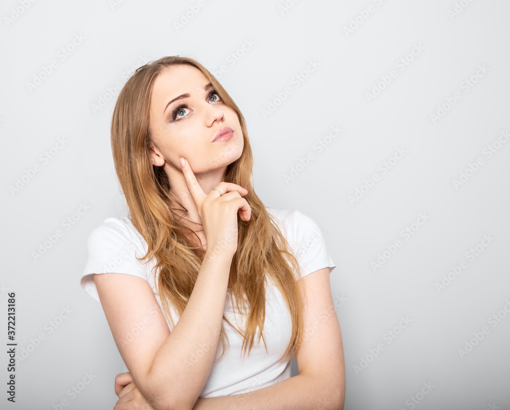 Thinking blond doubt young woman looking up and thinking on light blue background. Closeup portrait Thinking blond doubt young woman looking up and thinking on light blue background. Closeup portrait