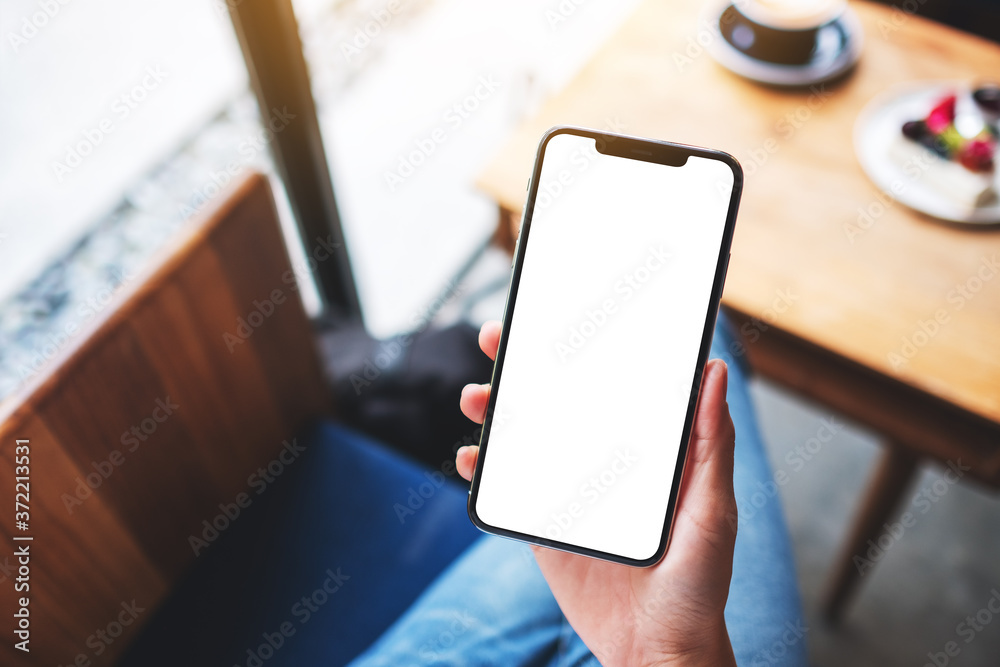 Mockup image of a woman holding mobile phone with blank white desktop screen in cafe Mockup image of a woman holding mobile phone with blank white desktop screen in cafe