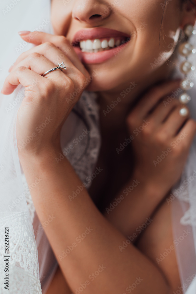 Cropped view of young bride in jewelry ring touching lace veil