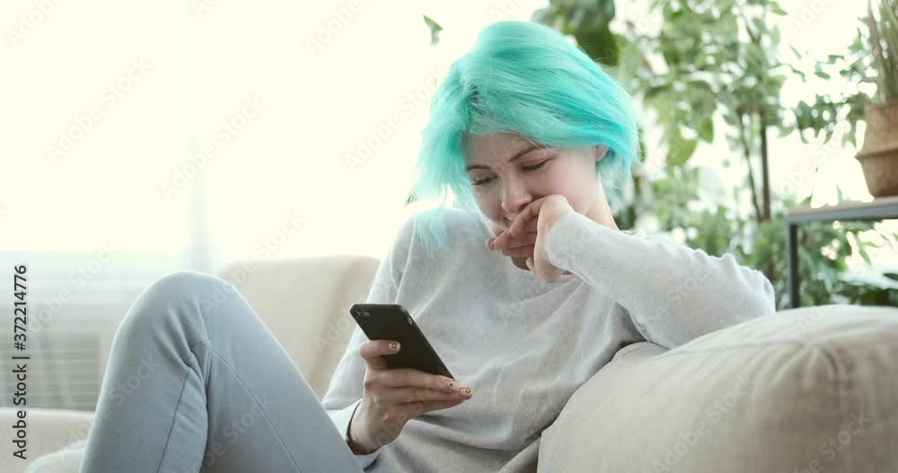 Happy woman with mint hairstyle using mobile phone on sofa at home Happy woman with mint hairstyle using mobile phone on sofa at home