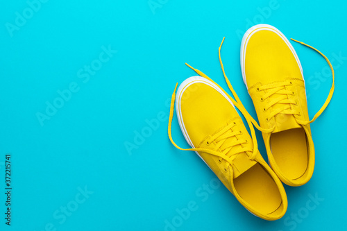 Minimalist flat lay image of yellow summer footwear over blue turquoise background with copy space. Top view photo of pair of yellow untied sneakers.