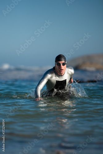 Obraz na plátně Athlete in wetsuit emerging from the ocean after a swim.