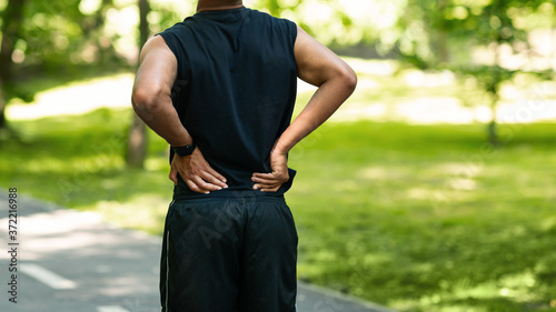 Black guy having back pain during his morning run at park, copy space © Prostock-studio