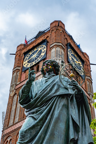 The Nicolaus Copernicus monument by Christian Friedrich Tieck unveiled in 1853 in Torun, Poland. The statue with the mask on beacause the virus pandemic. Brick tower of Thorn town hall in background.