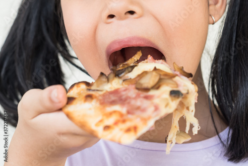 cute little girl holds piece of pizza  hungry student opens mouth wide while sees delicious slice of pizza  wants to eat  positive woman with junk food  people and eating  people and snack concept.