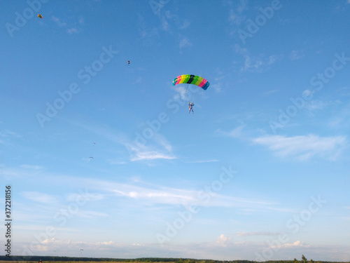 A skydiver with a bright multicolored parachute flies against the background of a blue sky with white sparse clouds