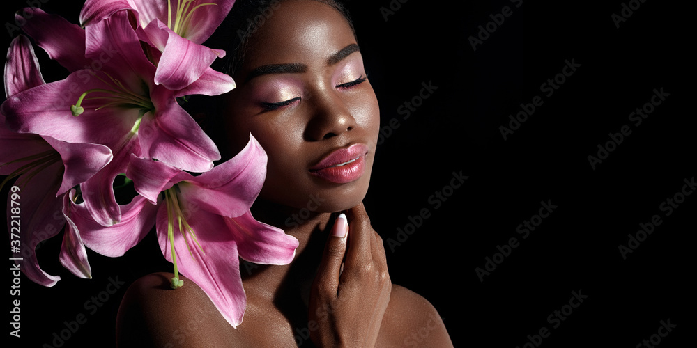 Tableau sur plexiglas avec Beauty portrait of young African American model with pink art make up posing with lily flowers isolated on black background. #372218799