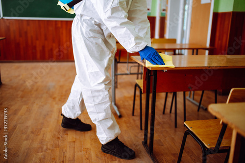 A man from disinfection group cleans up the desk at school with a yellow rag. Professional worker sterilizes the classroom to prevent covid-19 spread. Healthcare of pupils and students concept.