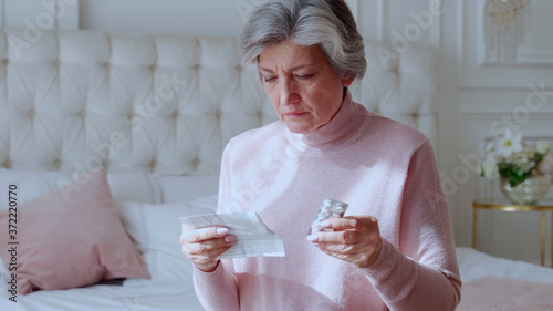 Fotografie An elderly woman with tablets in her hands and reads a prescription medication